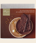 Bio Edelbitterschokolade mit Karamellstückchen und Salz – Tafelschokolade von Confiserie Berger, 90 g, freigestellt vor cremefarbenem Hintergrund